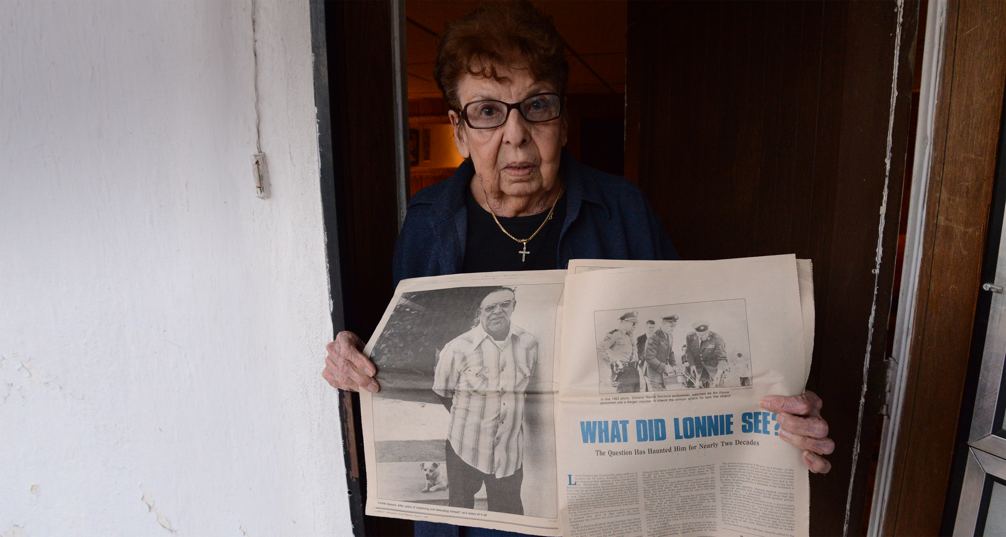 An elderly woman holding a newspaper about a UFO siting.
